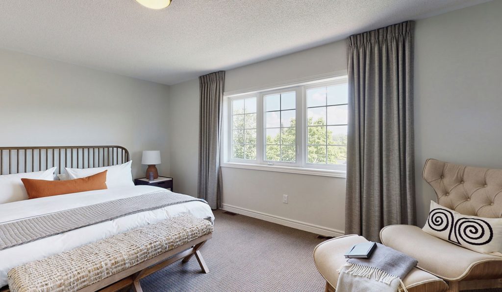 Picture Homes Model Home - Bedroom with Large King Bed and Comfortable Chair Beside Window